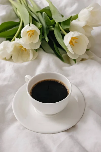 Tasse Kaffee und weiße Tulpen auf dem weißen Bett — Stockfoto