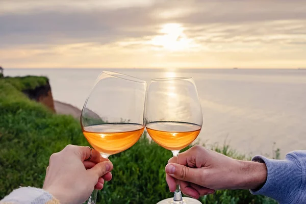 Paar klingelt mit zwei Gläsern Rosenwein bei Sonnenuntergang mit Blick auf das Meer. — Stockfoto