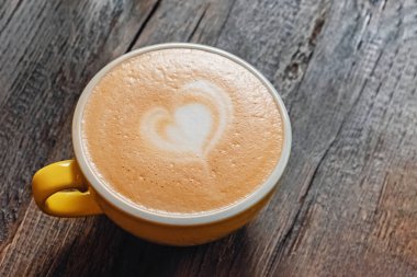 Sarı kapuçino ve ahşap masa üzerinde latte sanatı.
