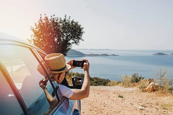 Man taking picture with smarphone from open window of a car stopped roadside — Stock Photo, Image