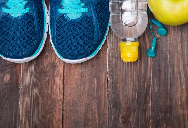 Sneakers, water, earphones  and apple on wooden background, top — Stock Photo, Image