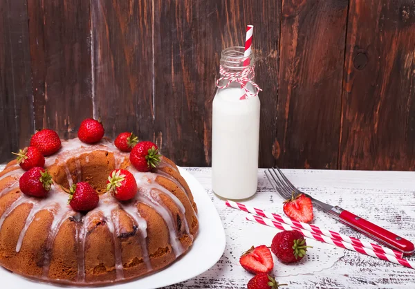 Delicious glazed cake with strawberry and bottle of milk — Stock Photo, Image