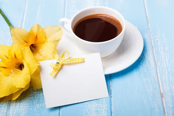 Yellow flower, coffee and empty card on blue wooden background — Stock Photo, Image