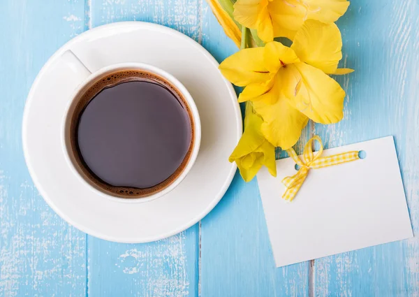 Tasse Kaffee, gelbe Blumen und leere Papierkarte auf blauem Holz — Stockfoto