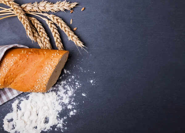 Bread, wheat ears and flour on the black background — Stock Photo, Image