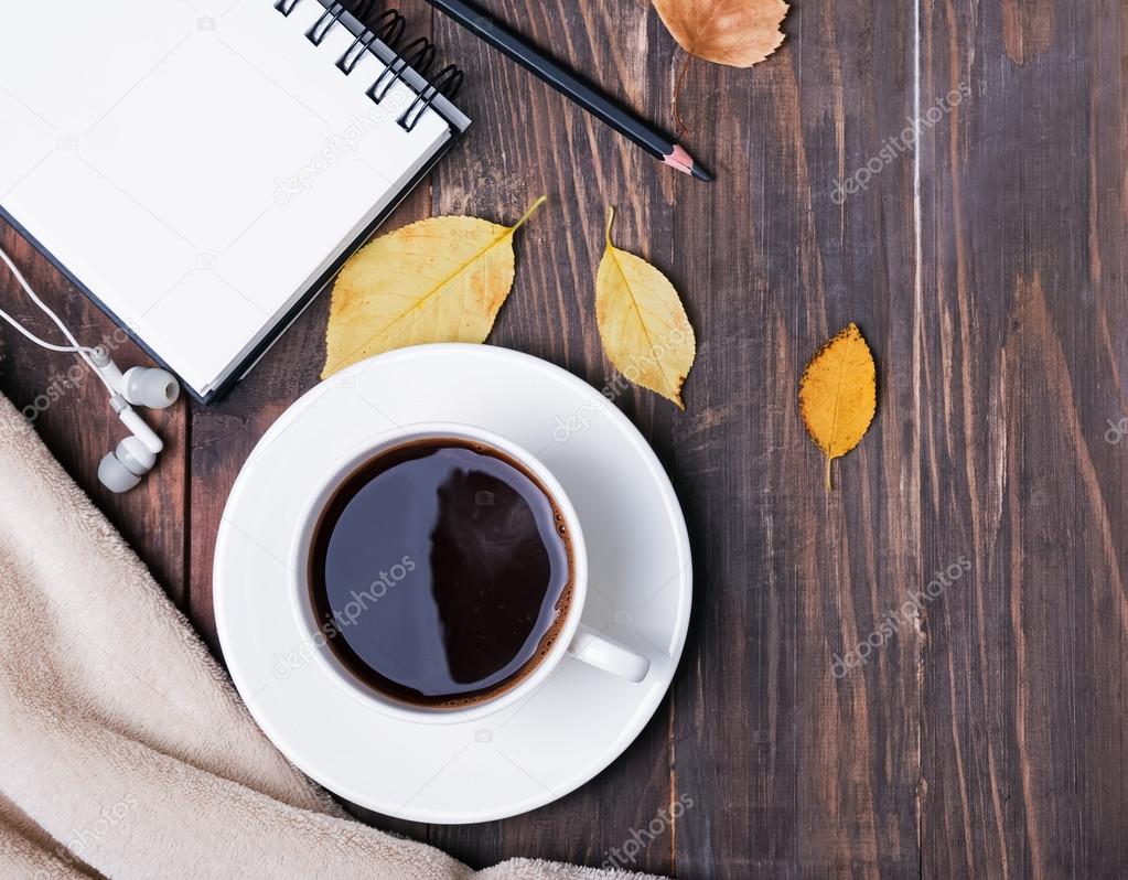 Coffee, notepad, pensil and autumn leaves on the wooden backgrou