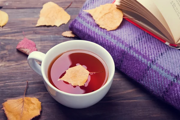 Çay, sonbahar yaprakları ve bir battaniye ahşap masa var