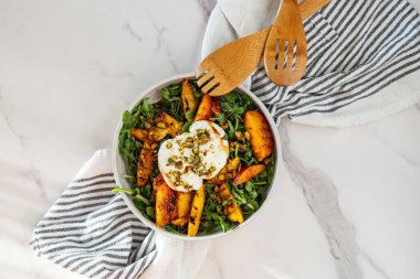 Taze roka içeren canlı bir salata ızgara şeftali, kremalı burata ve fıstık serpiştirilmiş..