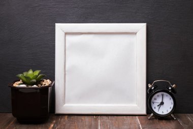 Blank white frame, alarm clock and succulent plant.