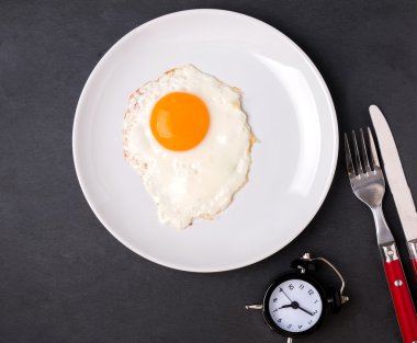 Fried egg on the plate, fork, knife and alarm clock 