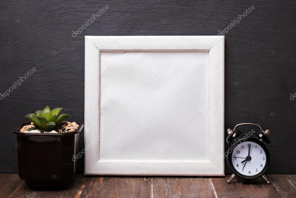 Blank white frame, alarm clock and succulent plant.