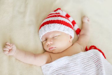 Örgü şapkalı şirin bebek yatakta uyuyor.