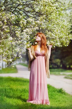 Güzel rüya gören kızıl saçlı kadın bahar zamanı çiçek açan kiraz ağacının yanında.  