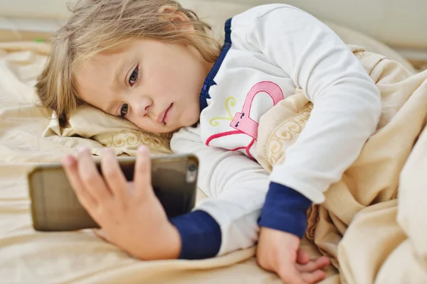 Menina na cama com smartphone — Fotografia de Stock