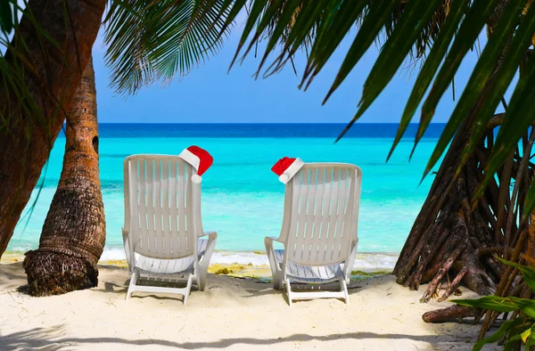 Liegestühle am tropischen Strand und Weihnachtsmann rote Weihnachtsmütze — Stockfoto