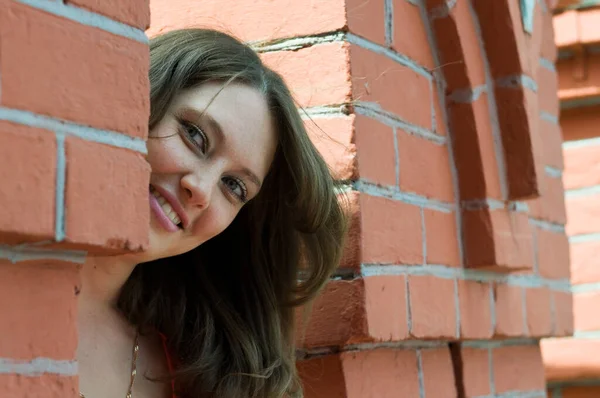 Smiling pretty young woman posing against brick wall — Stock Photo, Image