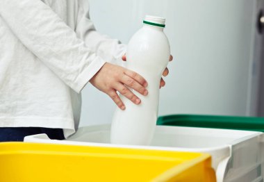 Çocuk boş plastik şişeyi üç çöp kutusundan birine atıyor.