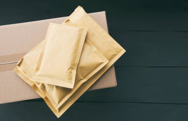 Tahta masanın üzerinde dört farklı boyutta kağıt zarf ve karton kutu var.