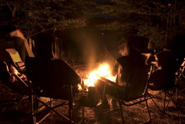 Gençler şenlik ateşinin etrafında oturup konuşuyorlar ve şarkılar söylüyorlar.