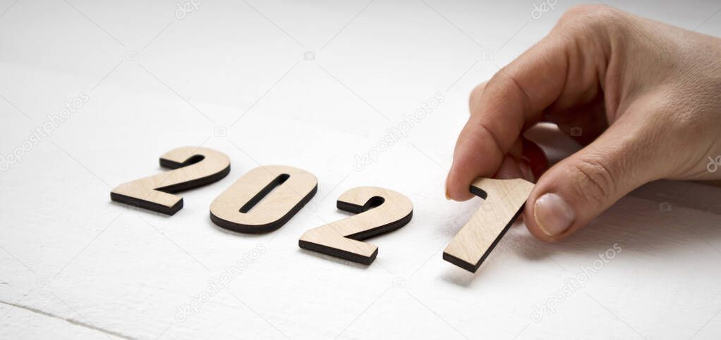 New Year 2021 concept. Female hand putting  wooden numbers 2021 on the wooden table