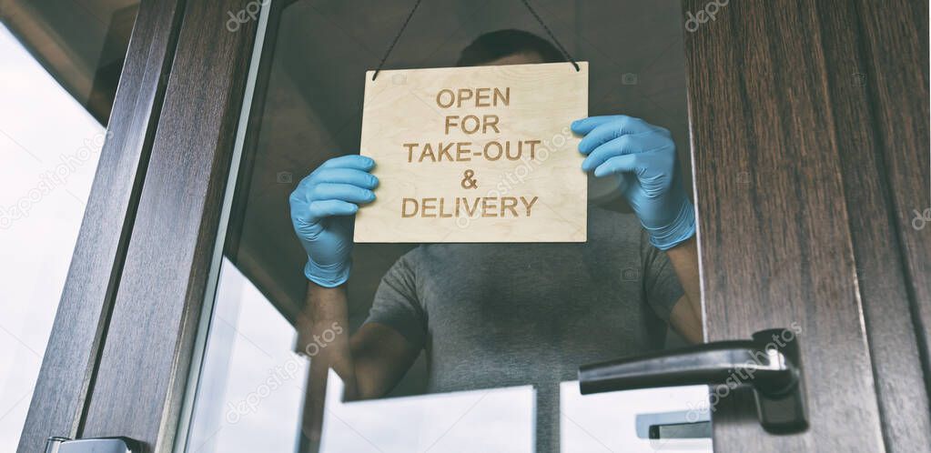 Man holds the wooden sign with text: Open for take-out and delivery