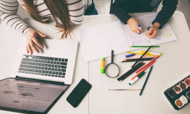 Annesi dizüstü bilgisayarla çalışırken çocuk resim çiziyor.