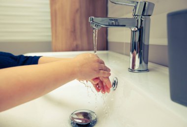 Çocuk suyun altında ellerini sabunla yıkıyor.