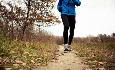 Genç adam sonbahar parkında koşuyor.