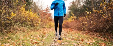 Genç adam sonbahar parkında koşuyor.