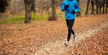 Genç adam sonbahar parkında koşuyor.