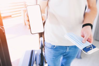 Bir elinde dijital aşı sertifikası, pasaport, maske ve bilet için boş yeri olan cep telefonunu tutan adam.