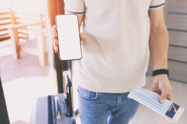 Bir elinde dijital aşı sertifikası, pasaport, maske ve bilet için boş yeri olan cep telefonunu tutan adam.