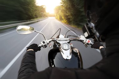 Motosikletli, akşamleyin boş asfalt yolda gidiyor.