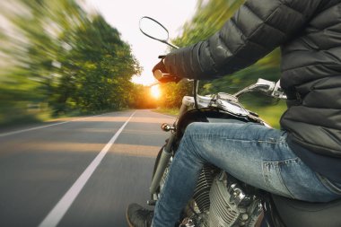 Motosikletli, akşamleyin boş asfalt yolda gidiyor.