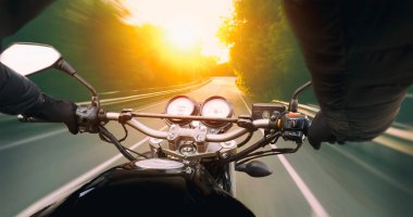 Motosikletli, akşamleyin boş asfalt yolda gidiyor.