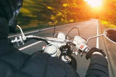 Motosikletli, akşamleyin boş asfalt yolda gidiyor.