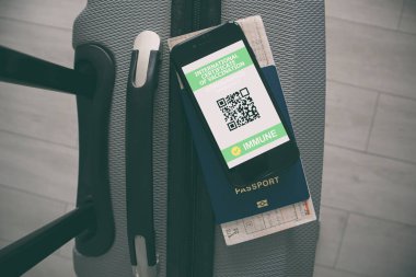 Bavuldaki cep telefonu ve ekrandaki aşı sertifikasının sağlık pasaportu.