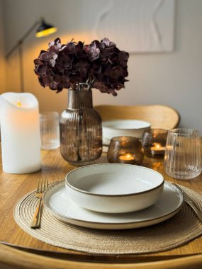 Cam eşyalar ve vazoyla ahşap masa seti şık bir akşam atmosferi yaratıyor. Mumlar, çiçekler ve rahat iç aydınlatmalı modern ev dekoruyla zarif, sıcak bir yemek masası..