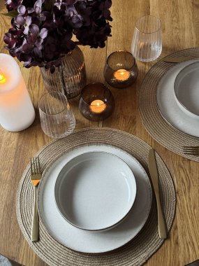 Cam eşyalar ve vazoyla ahşap masa seti şık bir akşam atmosferi yaratıyor. Mumlar, çiçekler ve rahat iç aydınlatmalı modern ev dekoruyla zarif, sıcak bir yemek masası..