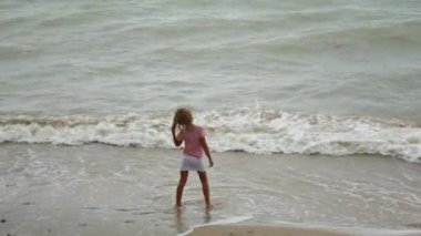 Bir çocuk yağmurda deniz kıyısında yürüyor.