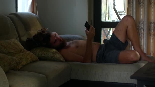 Junger Mann legt sich zum Schlafen aufs Sofa und legt das Telefon weg — Stockvideo