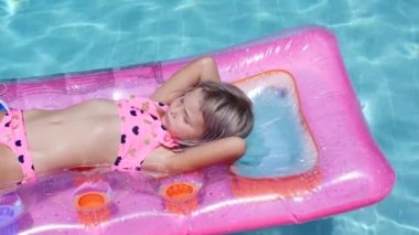 Sarışın kız şişme yatakta havuzda yüzüyor.