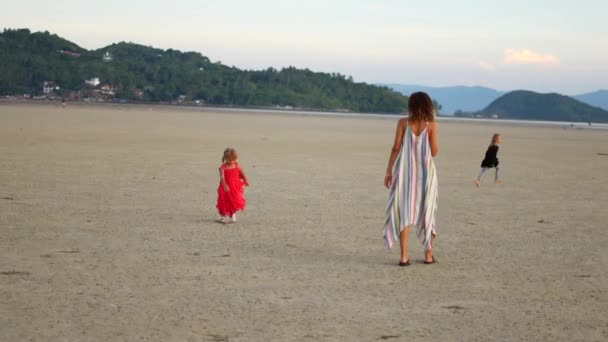 Η μαμά και οι κόρες περπατούν στην παραλία την αυγή. — Αρχείο Βίντεο