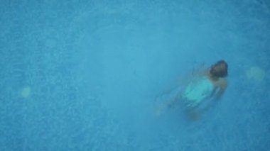 Kız çocuğu havuzda yüzüyor, yukarıdan havuz manzaralı.