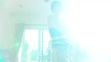 Göz kamaştırıcı ve ışıl ışıl bir karede, 30 'lu yaşlarının ortasında, şık kısa saç stili olan güzel ve çekici bir kadın oturma odasında zarif bir şekilde dans ediyor. Altın güneş ışığı pencereden akıyor.