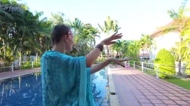 Dinamik ve estetik açıdan tatmin edici bir çekim, yüzme havuzunda zarif bir şekilde dans eden kısa saçlı kızın alt vücut ve kol hareketlerine odaklanır. Uçan mavi kimono elbisesi