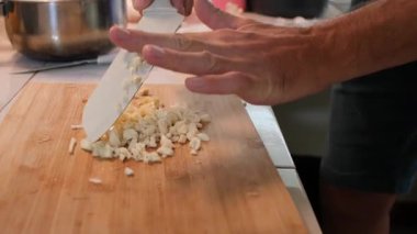 Ayrıntılı bir yakın çekim, 38 yaşındaki kısa sakallı yetenekli Avrupalı bir adamın mutfağındaki tahta kesme tahtasındaki taze sarımsak karanfillerini titizlikle doğramasına odaklanıyor. Sahne