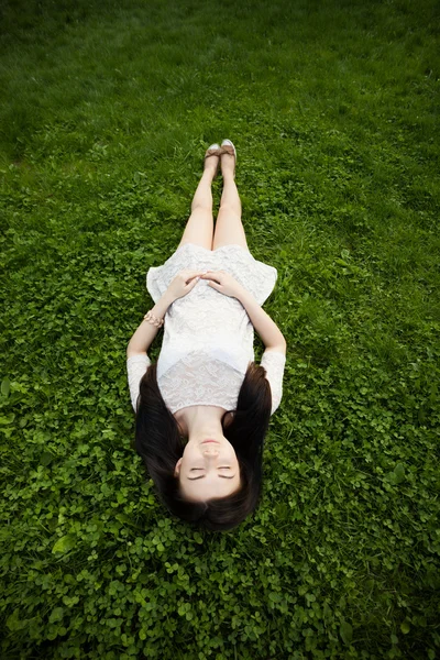 Young white girl in sundress lying on green grass in garden — Stock Photo, Image