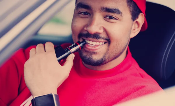 Young black guy smoking e-cig vaporizer in car — Stok fotoğraf