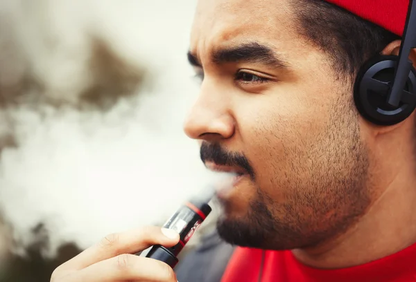 Young black man smoking e-cigarette vaporizer device — Stok fotoğraf